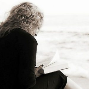 A woman sits in the sand at the beach reading a book