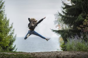 A woman with a backpack in the forest jumps for joy.