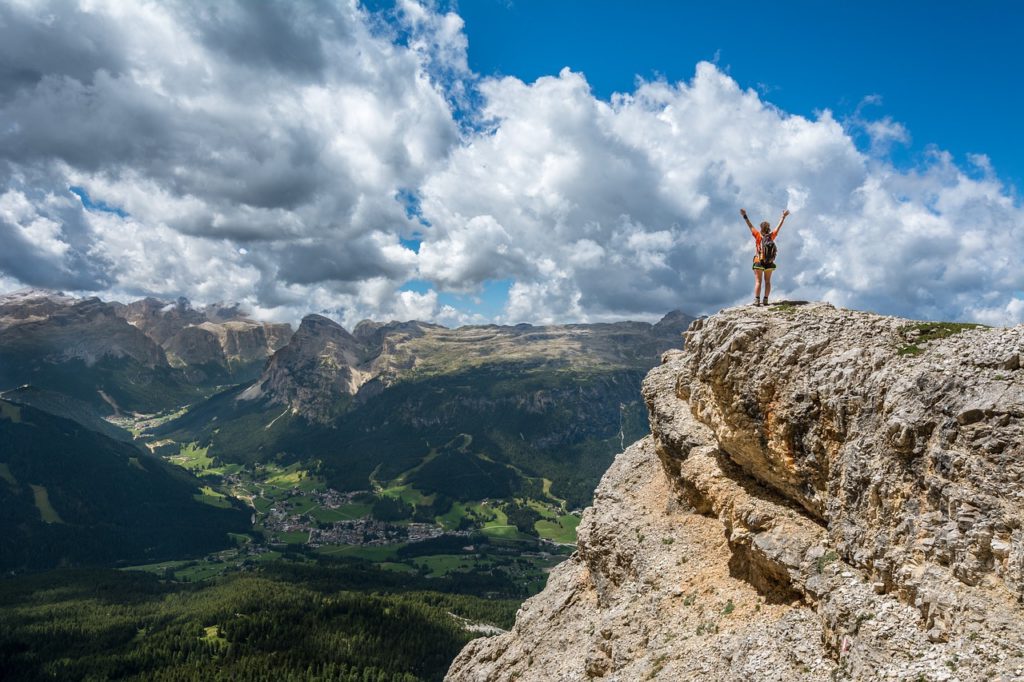 Woman standing on top of a mountain overlooking a gorgeous mountain view with fluffy clouds