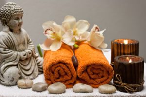 A budha figurine overlooks two orange towels rolled with flowers draped on top 