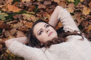A woman looking deep in thought lies on the ground over top of orange and brown fallen leaves