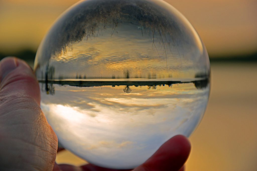 A hand holds a clear sphere with a snowy landscape reflecting in it.