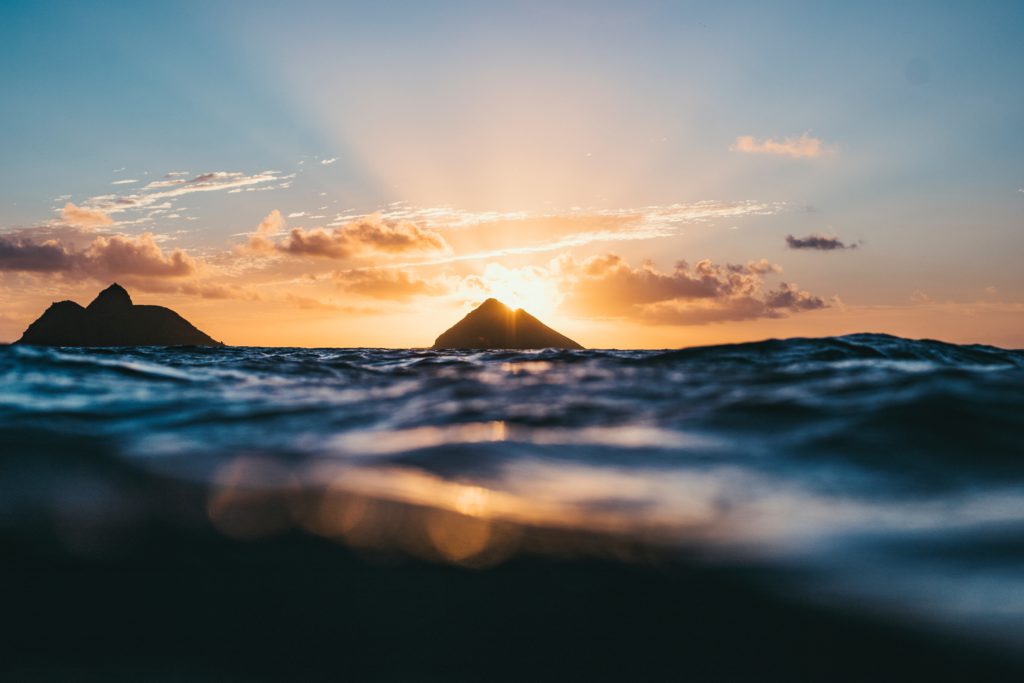 This beautiful photo of mountains protruding out of water with the sun setting behind is by Ryan Pernofski from UnSplash