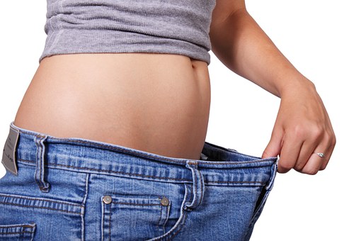 A woman holding out the waist of her pants. She has obviously lost weight.