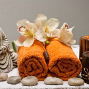 A budha figurine overlooks two orange towels rolled with flowers draped on top